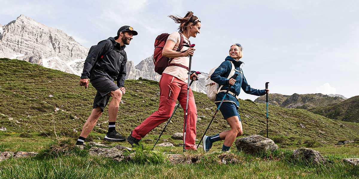 Zwei Frauen und ein Mann in Wanderoutfits und Wanderstöcken in den Bergen