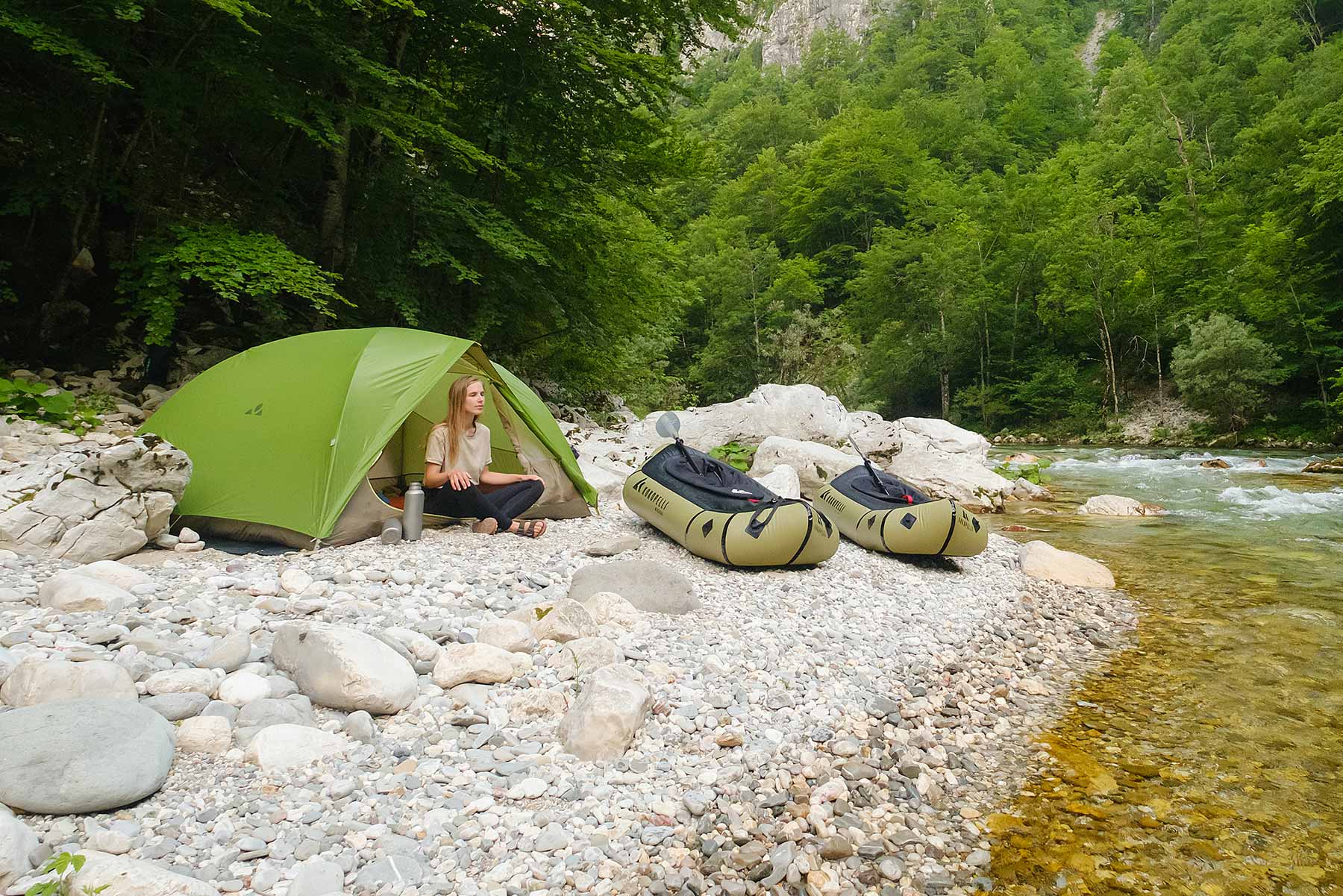 Woman sitting in front of her tent, two boats on the shore in front of her