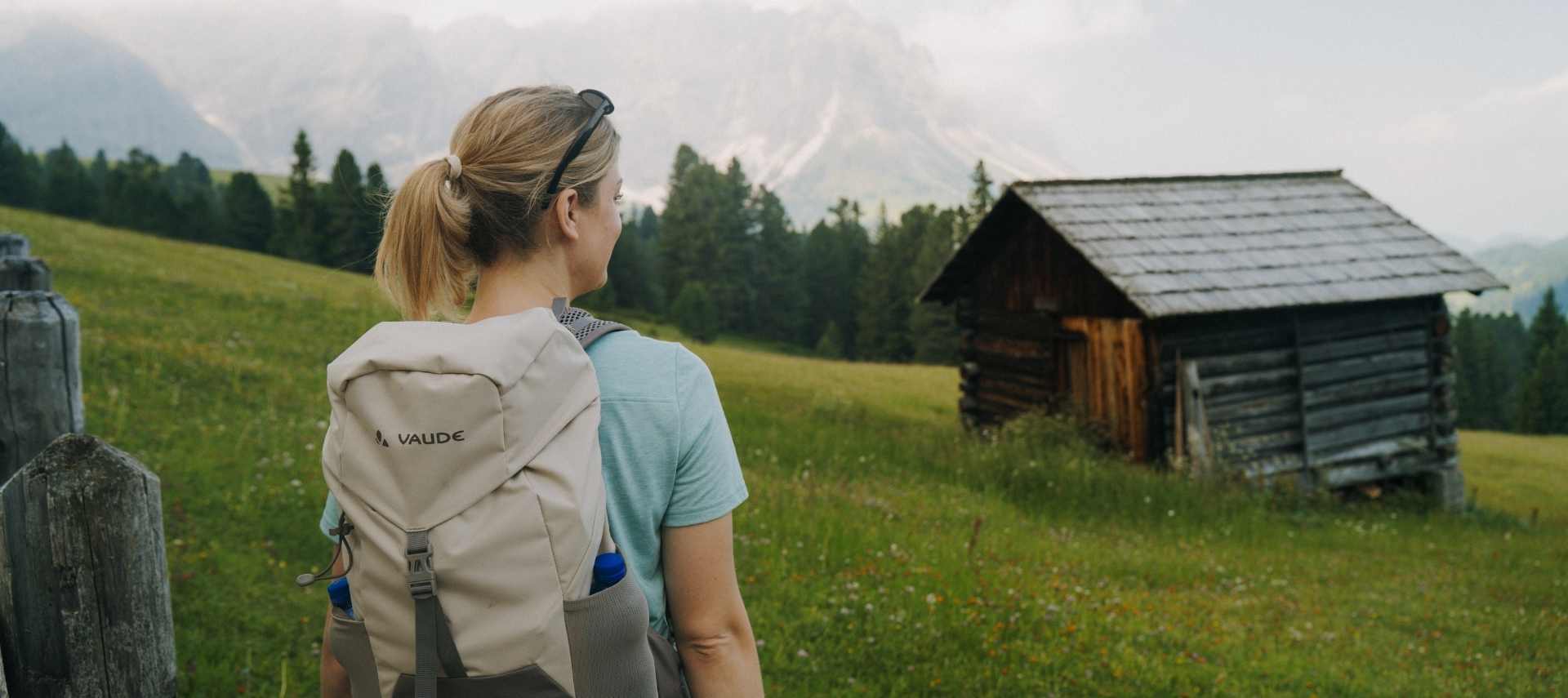 A young woman with a VAUDE backpack looks at the mountains