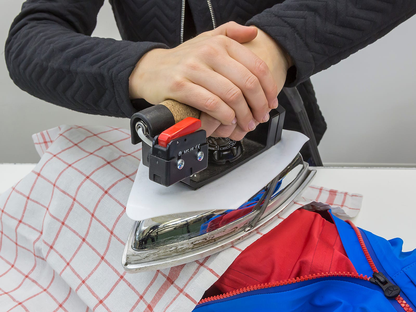 Durch ein Tuch hindurch wird eine Jacke gebügelt