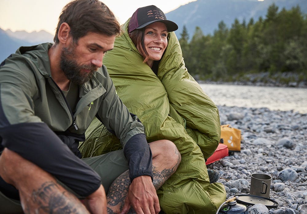 Couple assis dans un sac de couchage au bord d'une rivière