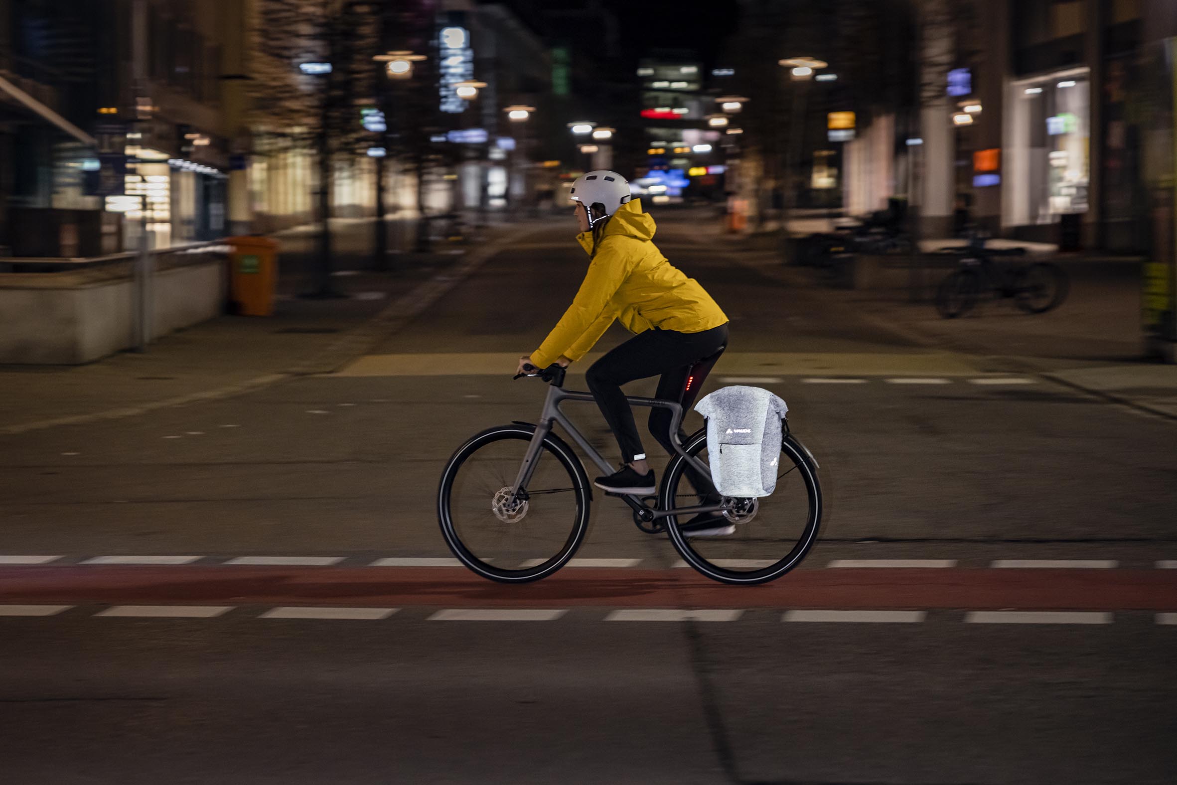 Eine Radfahrerin nachts in einer Stadt mit einer reflektierenden VAUDE Tasche am Gepäckträger