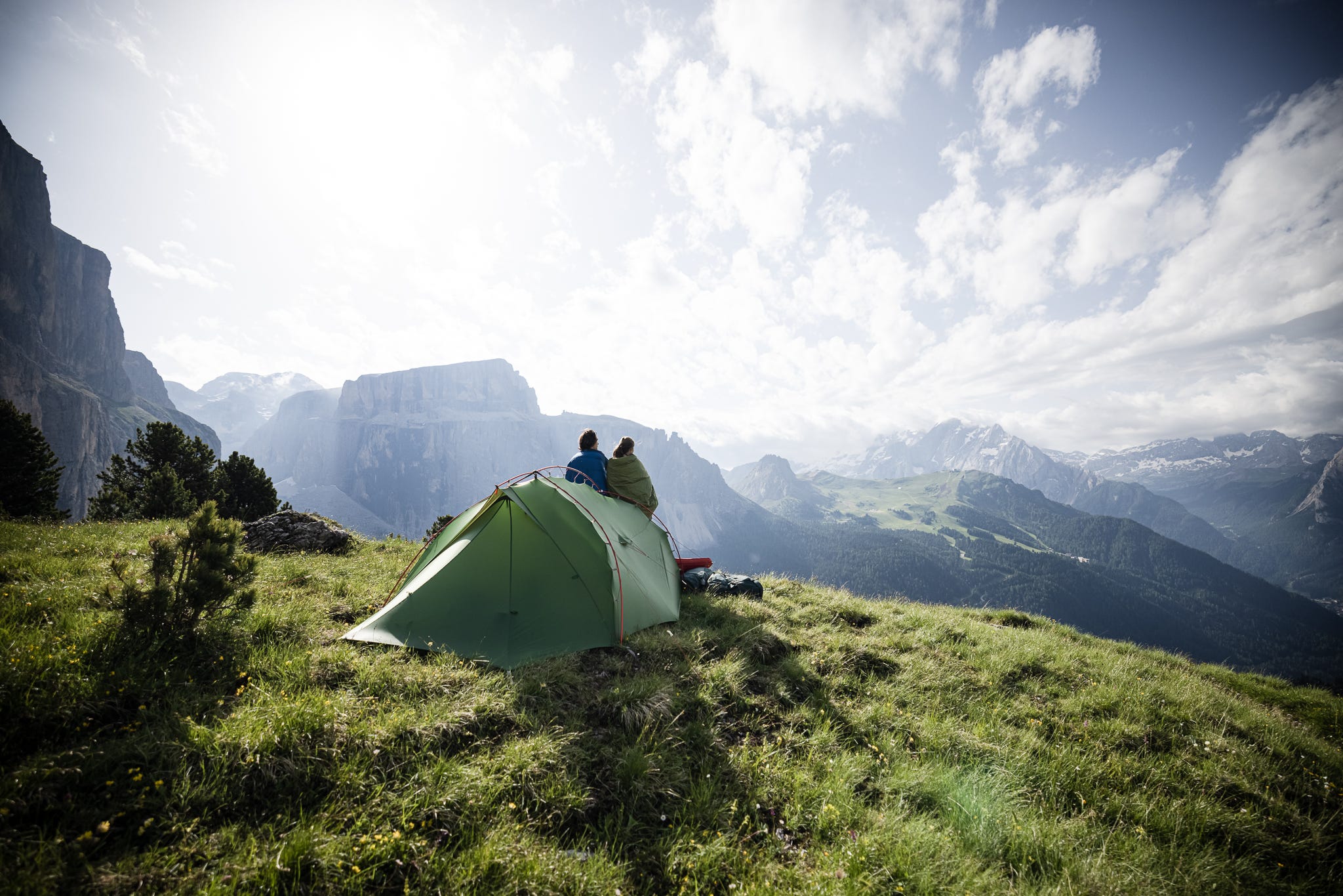 Ein Mann und eine Frau stehen vor ihrem VAUDE Zelt auf einem Berg und schauen ins Tal