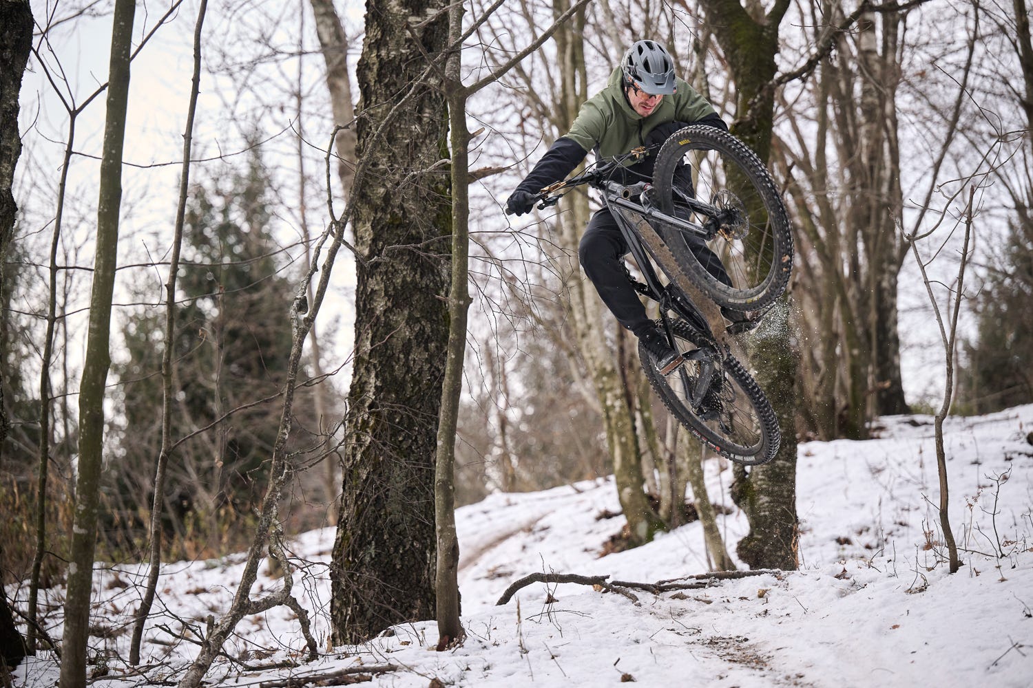 Ein Mountainbiker springt über einen verschneiten Trail