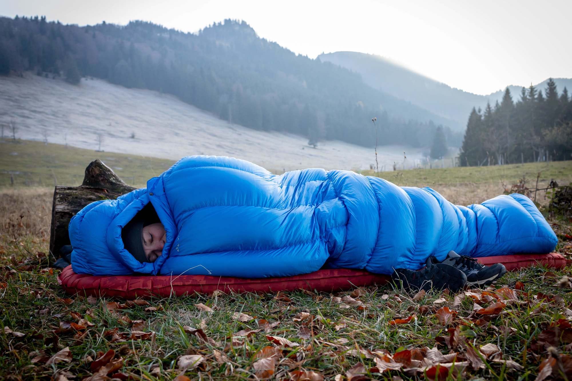 Eine Frau schläft gut eingepackt im Schlafsack unter freiem Himmel
