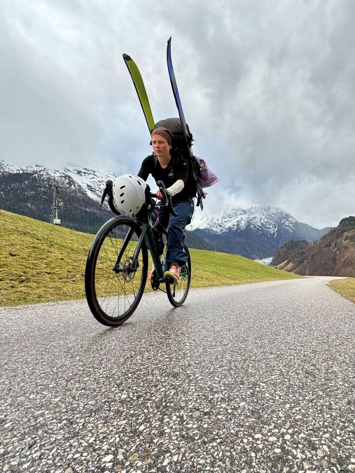 Frau mit Rucksack und Ski fährt auf Rennrad in den Bergen.