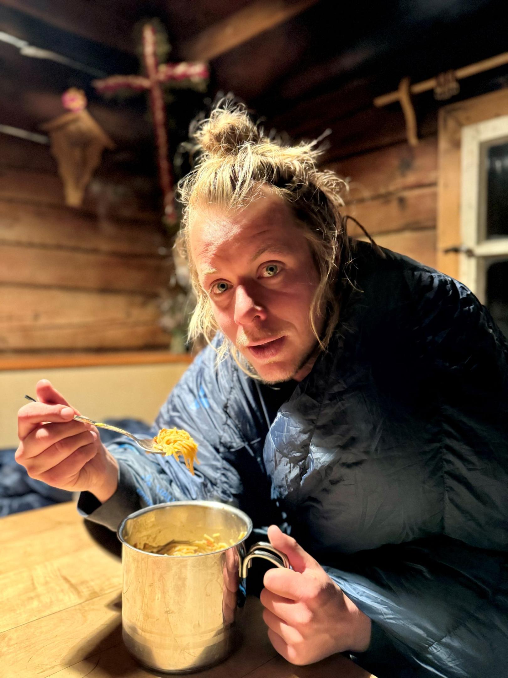 Ein Mann mit einem Schlafsack um die Schultern ist sein Abendessen auf der Alm.