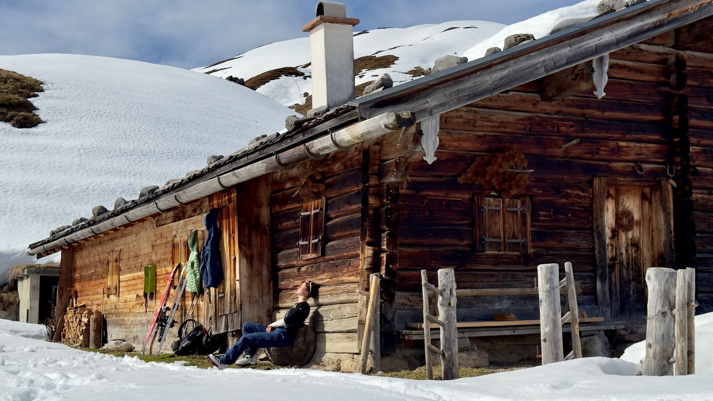 Frau sitzt vor Berghütte in der Sonne.