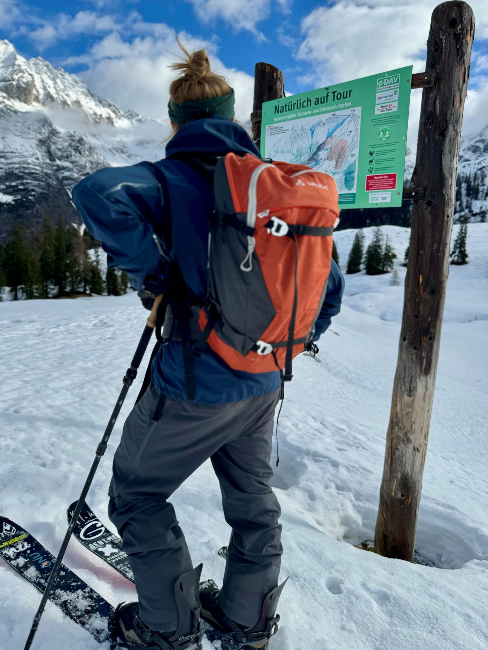 Snowboard-Tourengeher steht vor "Natürlich auf Tour" Schild des Deutschen Alpenvereins.
