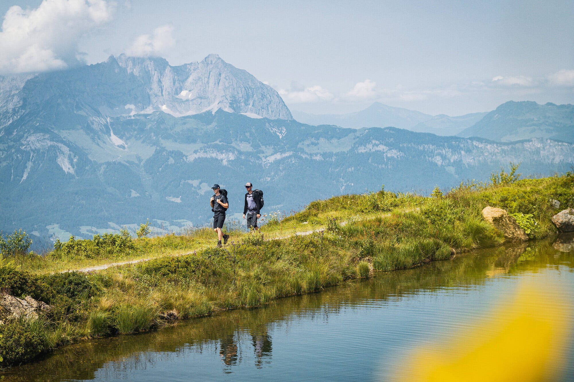 auf einem Wanderweg zwischen See und Bergen gehen zwei Wanderer