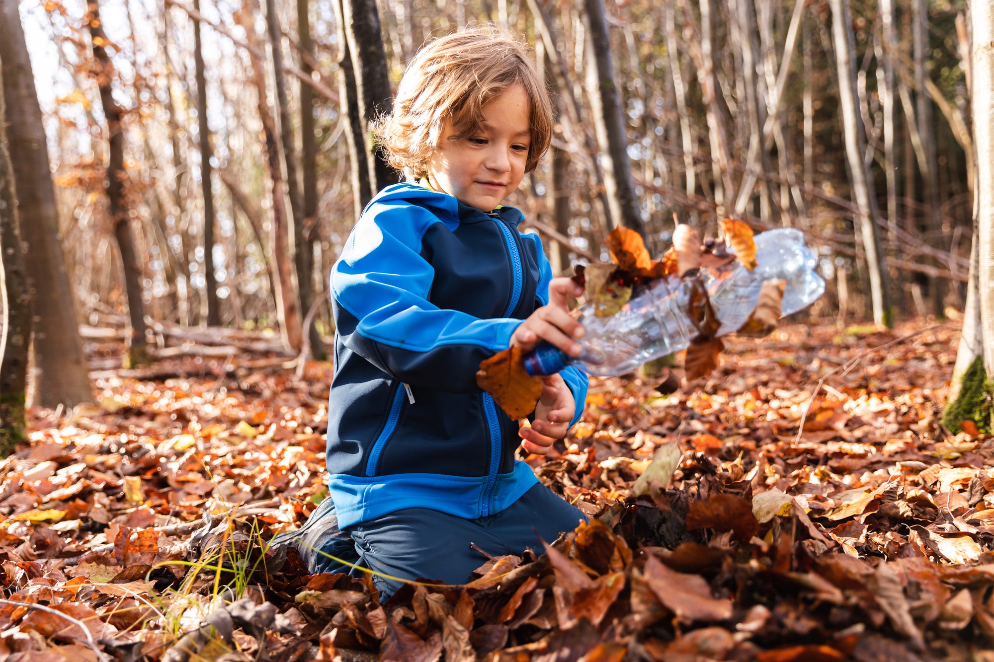 Kind findet alte Plastikflasche im Herbstlaub.