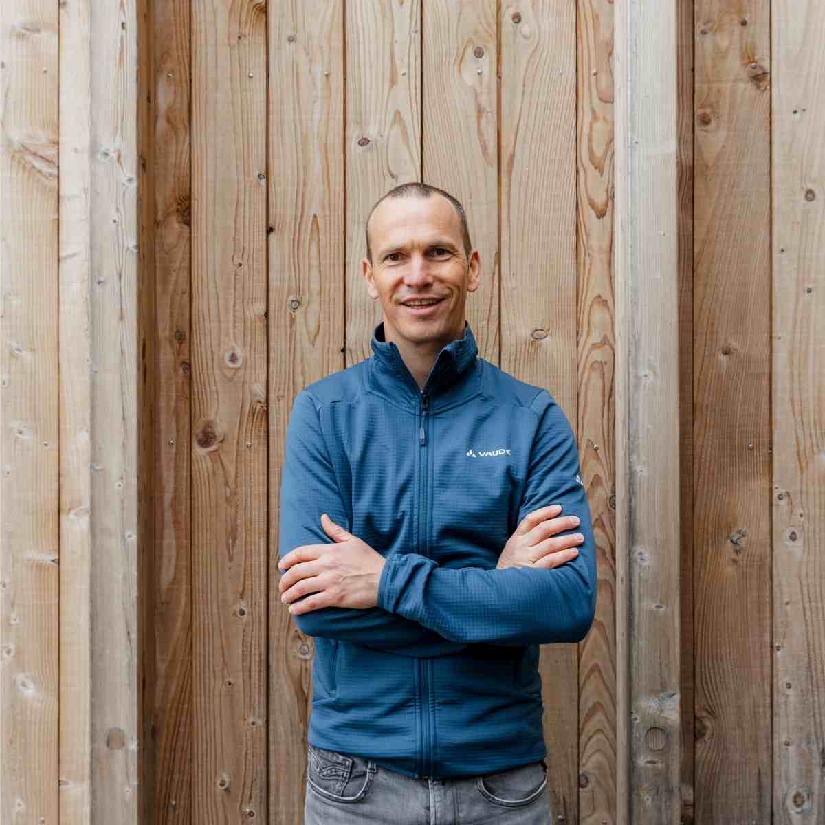 Michael, Mitarbeiter von VAUDE, steht vor einer Natur-Holzwand