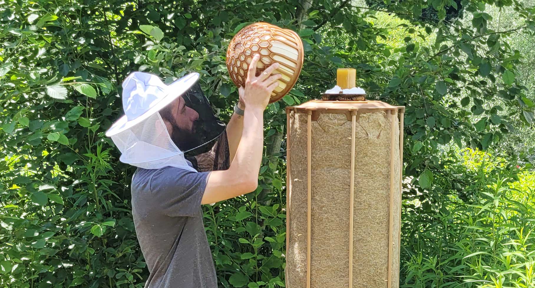 Man with bee hat next to beehive
