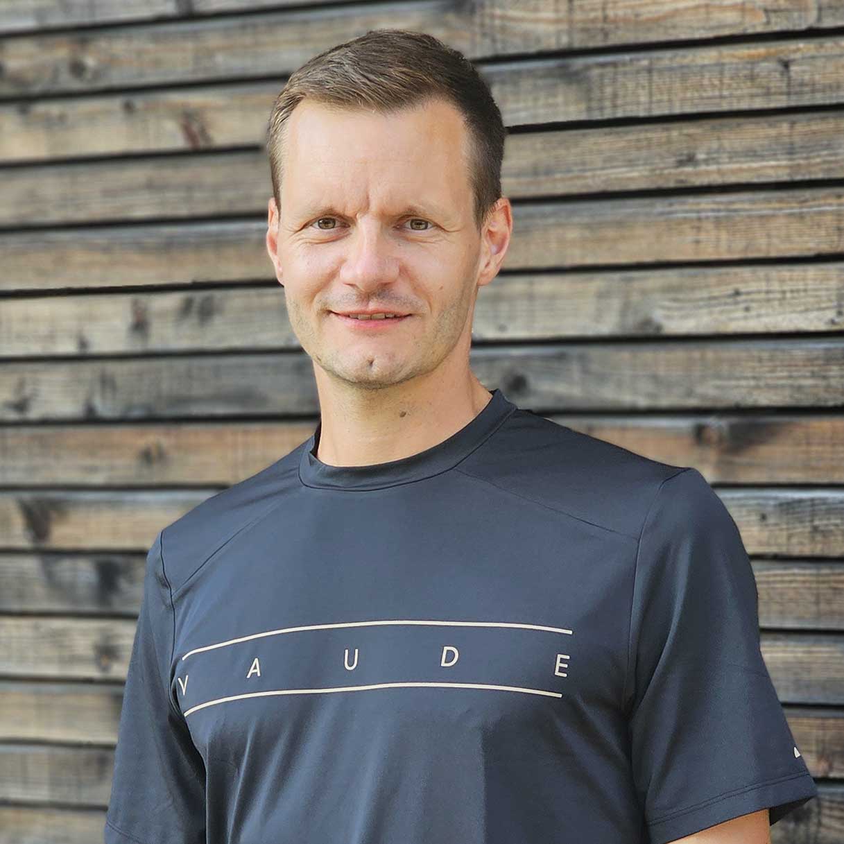 Michael, Mitarbeiter von VAUDE Michael, Mitarbeiter von VAUDE, steht vor einer Natur-Holzwand