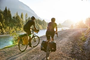 Ein Mann und eine Frau auf Gravelbikes auf einem Schotterweg neben einem Fluss